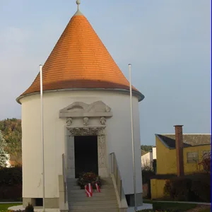 Runde weiße Kapelle mit rotem Kegeldach und steinernem Portal